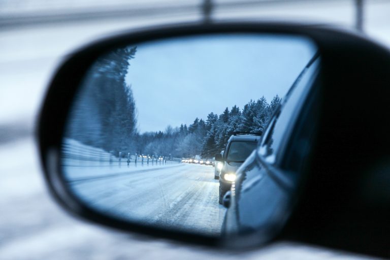 Genom en bils sidospegel ser man en bilkö på snötäckt väg