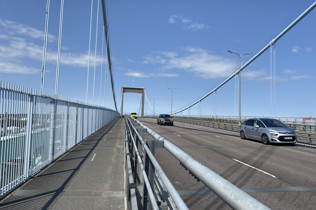 Två personbilar och en ambulans kör äver Älvsborgsbron. Pylonerna syns i bakgrunden och gång- och cykelbanan till vänster i bild.