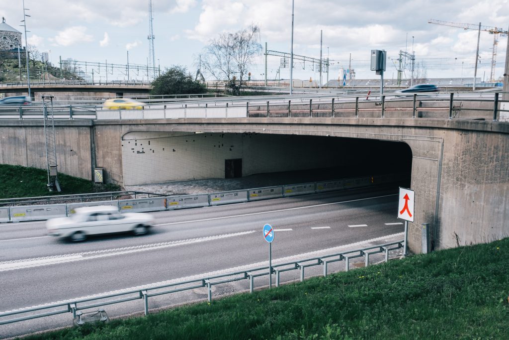 En personbils syns köra på E6 förbi Olskroksmotet. Skansen Lejonet syns i bakgrunden.